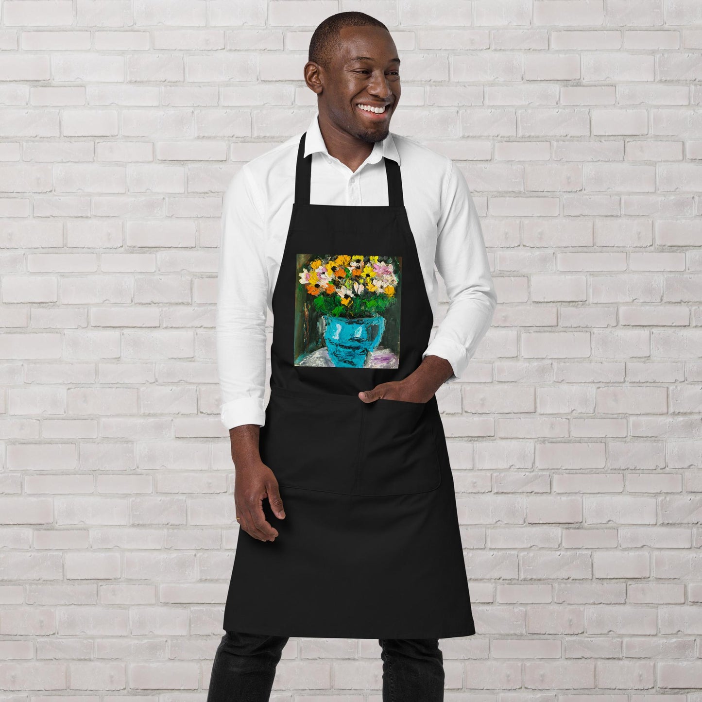 Tablier de cuisine artistique noir avec motif bouquet fleuri porté par un homme souriant.